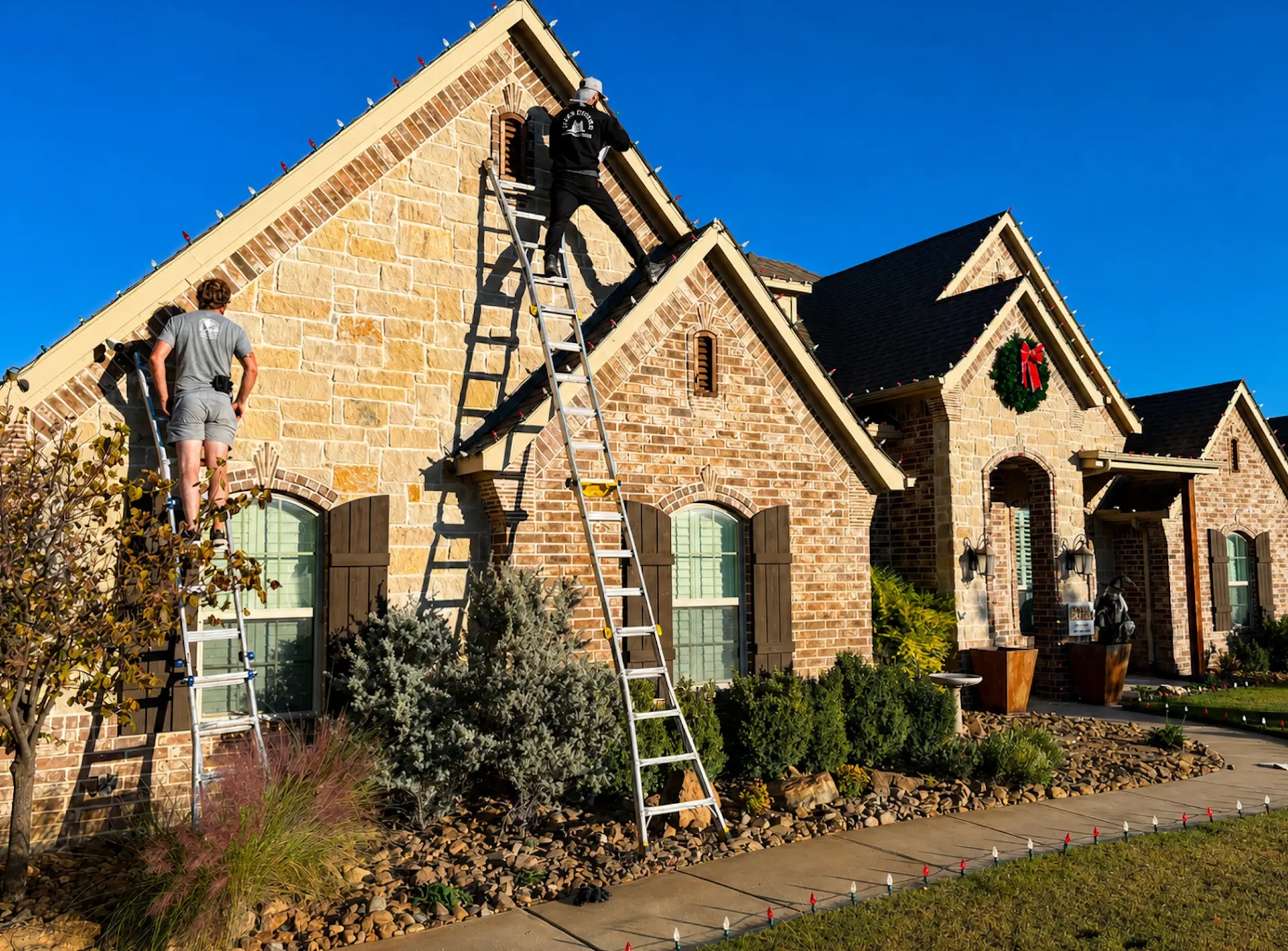 Jolly Icicles installers on ladders decorating a brick home in the Dallas–Fort Worth area