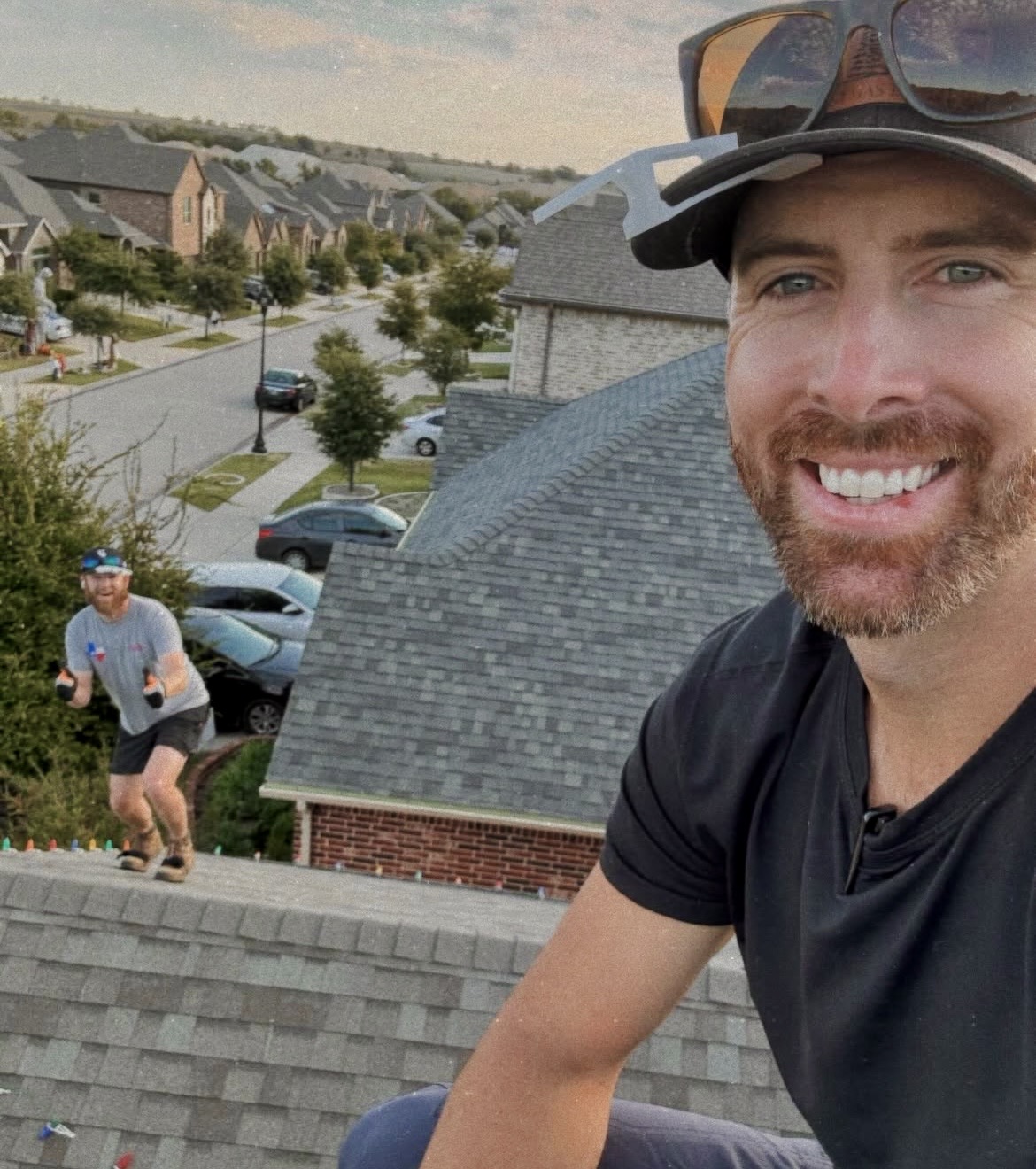 Two smiling Jolly Icicles installers on a roof above a DFW neighborhood