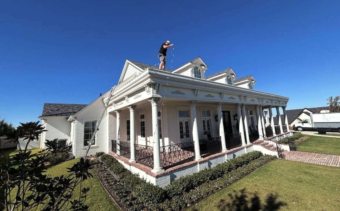 Jolly Icicles installer on the roof of a large white home in daylight